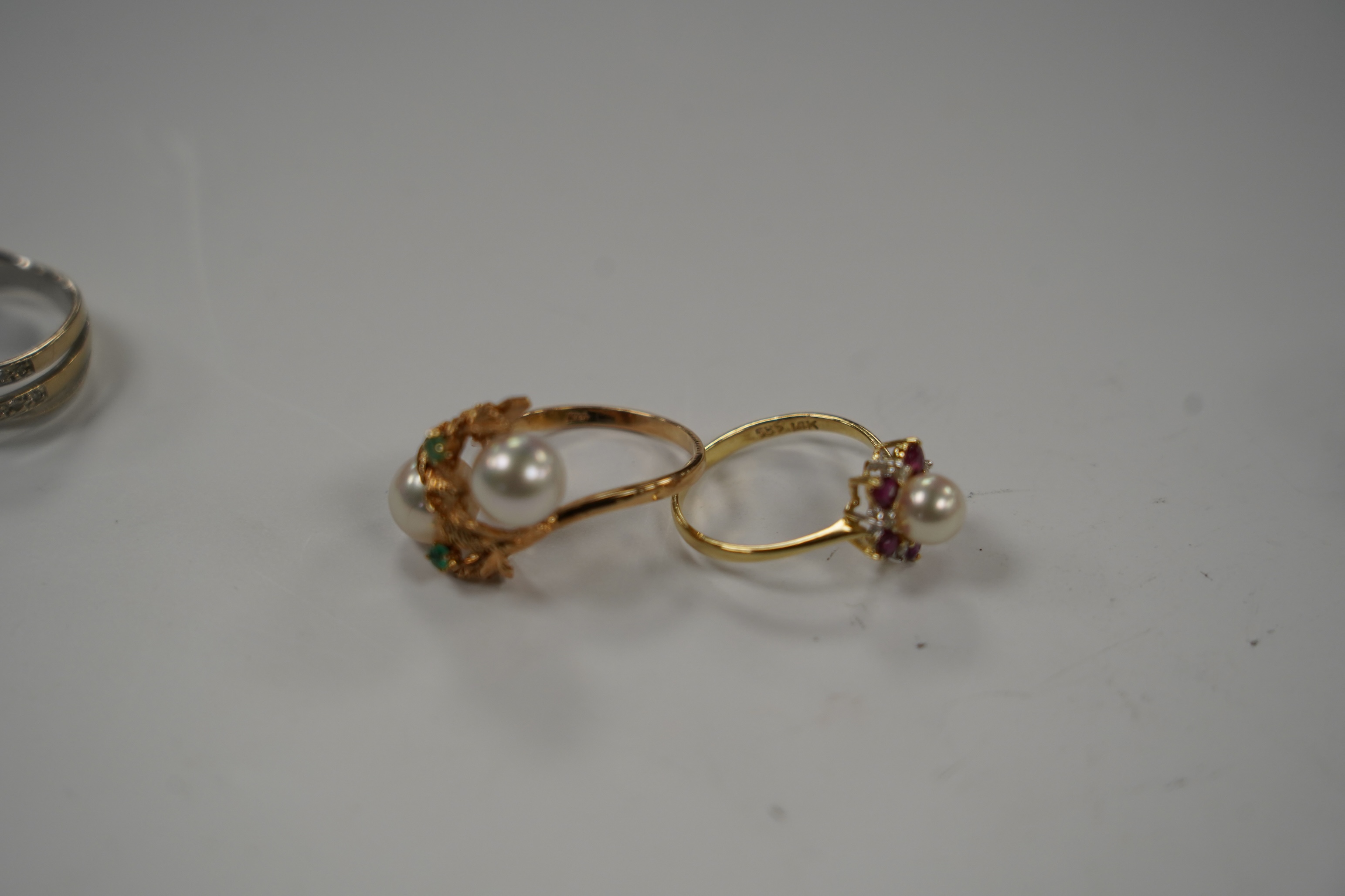 Two modern continental yellow metal and diamond chip set triple band cross over rings, size N, a 14k, ruby, diamond and cultured pearl set cluster ring, a 14k, two stone cultured pearl and a two stone emerald set ring.